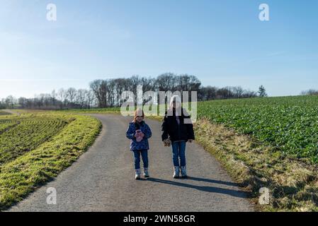 Due sorelle camminano su una strada di campagna in campagna in primavera Foto Stock