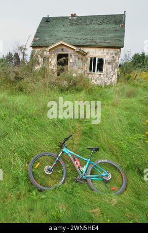 Mountain bike adagiata sul prato sovrastato di una vecchia casa abbandonata. Foto Stock