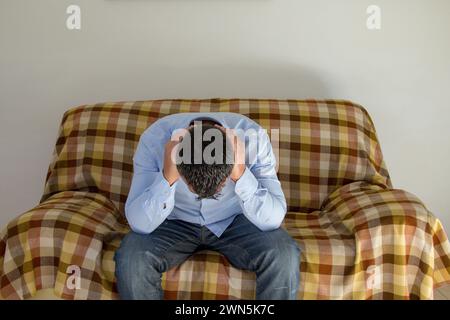Immagine di un uomo seduto su un divano mentre si copre le orecchie e non vuole sentire nessuno. Problemi di ansia e depressione. Foto Stock