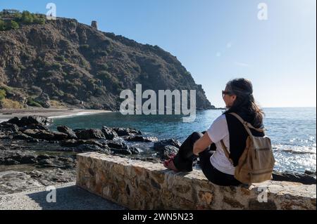 Donna di 50 anni che contempla la spiaggia di Currumbico a Almuñécar (Spagna) in una soleggiata mattina d'inverno Foto Stock