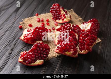 Un grande melograno con grandi semi maturi e succosi viene spezzato in pezzi su fondo di legno, e i chicchi di melograno sono sparsi. Foto Stock