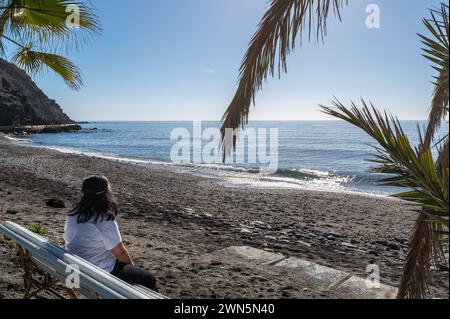 Donna di 50 anni che contempla la spiaggia di Cabria a Almuñécar (Spagna) in una soleggiata mattina d'inverno Foto Stock