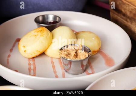 Colazione slava. Syrniki servito con marmellata di lamponi e latte condensato bollito. Primo piano con messa a fuoco morbida selettiva Foto Stock