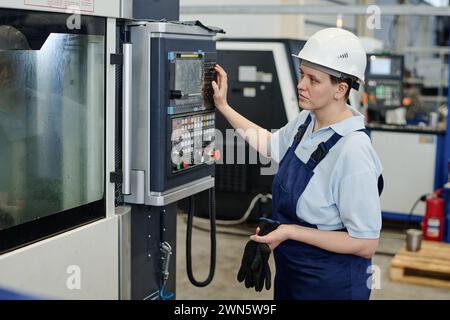 Lavoratrice di fabbrica moderna che indossa una macchina CNC funzionante in modo uniforme, spazio di copia Foto Stock