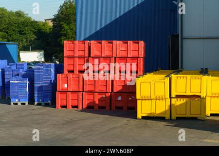 Una serie di contenitori di stoccaggio industriali dai colori vivaci sono meticolosamente impilati all'esterno di un magazzino sotto cieli limpidi. Foto Stock