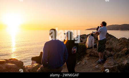 Persone che guardano il tramonto sull'Oceano Pacifico a Malibu, California, dalle scogliere sopra l'acqua, nel pomeriggio estivo mentre il sole tramonta lungo la costa Foto Stock