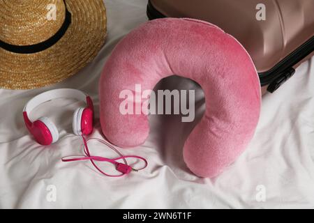 Cuscino da viaggio rosa, valigia, cappello e cuffie sul letto Foto Stock