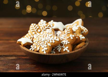 Gustosi biscotti di Natale con glassa nel recipiente su un tavolo di legno contro le luci sfocate Foto Stock