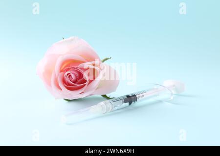 Cosmetologia. Siringa medica e fiore di rosa su sfondo azzurro Foto Stock