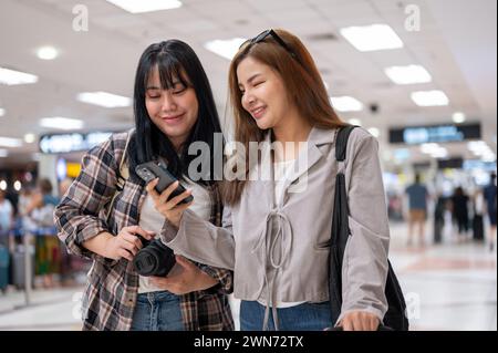 Due allegre ragazze asiatiche viaggiatrici passeggeri stanno parlando mentre camminano in aeroporto, viaggiando insieme. concetti relativi a persone e trasporti Foto Stock