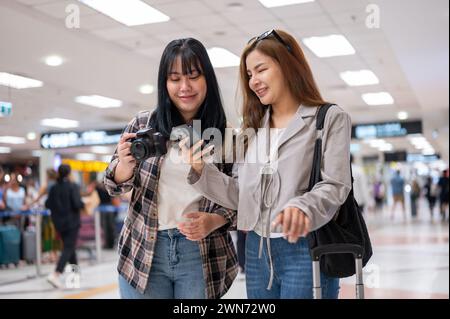 Due allegre ragazze asiatiche viaggiatrici passeggeri stanno parlando mentre camminano in aeroporto, viaggiando insieme. concetti relativi a persone e trasporti Foto Stock