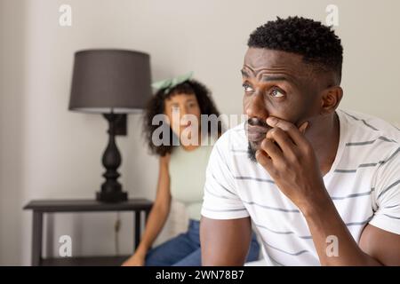 Un uomo afroamericano appare sconvolto a casa, con una giovane donna birazziale sullo sfondo Foto Stock