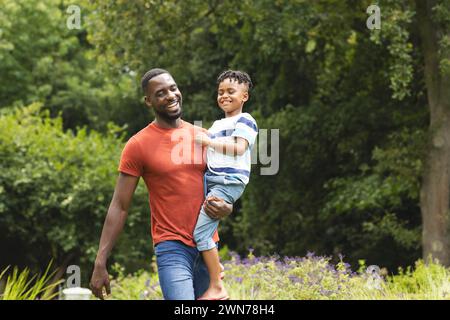 Il padre afroamericano porta suo figlio in una giornata di sole nel parco con spazio fotocopie Foto Stock