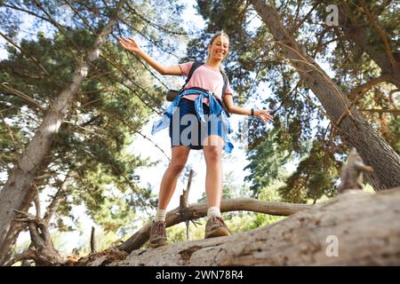 Giovane donna caucasica si bilancia su un tronco di albero caduto all'aperto durante un'escursione Foto Stock