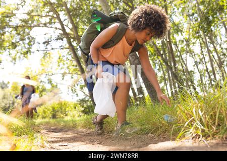 Una giovane donna birazziale raccoglie la spazzatura mentre fa trekking, promuovendo la tutela dell'ambiente Foto Stock