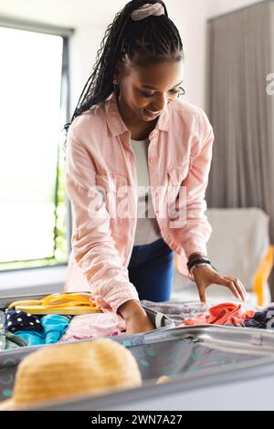 Una giovane donna afro-americana porta i vestiti in una valigia Foto Stock