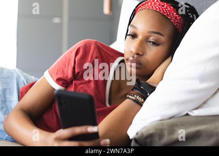 La giovane donna afroamericana si rilassa mentre naviga sul suo smartphone Foto Stock