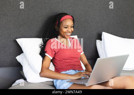 Una giovane donna afroamericana lavora sul suo portatile con un sorriso Foto Stock