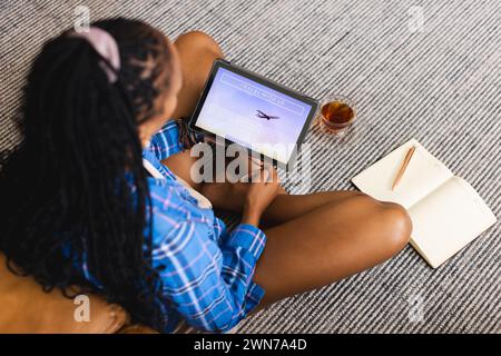 Una donna concentrata prenota le vacanze mentre studia sul suo tablet. Foto Stock