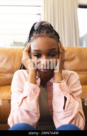 Una giovane donna afroamericana che si sente triste, riposa la faccia tra le mani Foto Stock