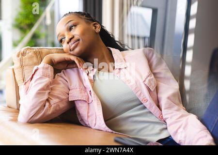 Una giovane donna afroamericana si rilassa con cura su un divano Foto Stock