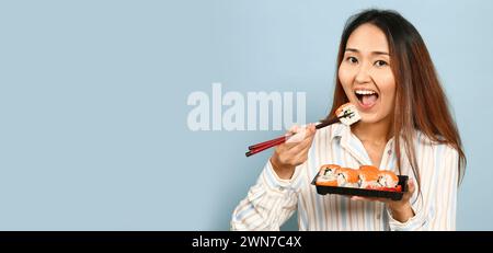 Donna asiatica che mangia sushi su sfondo azzurro con spazio per il testo Foto Stock