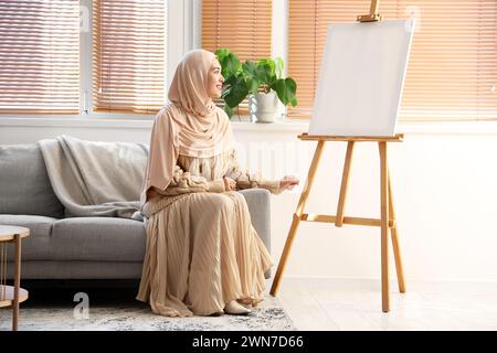 Giovane donna musulmana seduta sul divano a casa Foto Stock