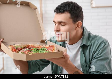 Giovane uomo che tiene in mano una scatola di cartone con gustosa pizza a casa Foto Stock