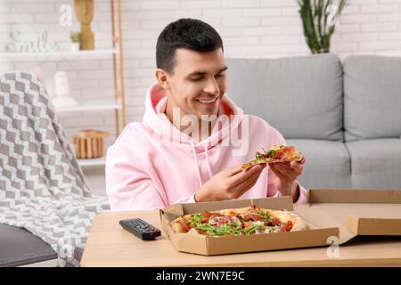 Giovane con un pezzo di gustosa pizza a casa Foto Stock
