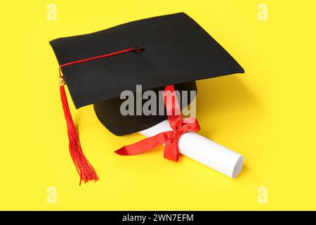 Cappello di laurea e diploma su sfondo giallo Foto Stock