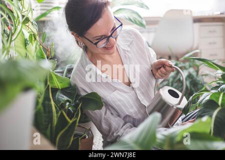Una giovane donna annaffia e si prende cura di una pianta di casa Banana e sansiveria. Foto Stock