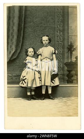 Originale e affascinante carte de visite vittoriana (biglietto da visita o CDV) di 2 sorelle dall'aspetto dolce, - giovani ragazze vittoriane, bambini vittoriani, che sembrano seri, indossando bellissimi camici con maniche corte e dettagli intrecciati capelli in boccoli avvolti sul lato della testa. A cura dell'artista fotografico Kitchen, 25 Argyle St Birkenhead, Liverpool, Inghilterra, Regno Unito. Intorno al 1864 Foto Stock