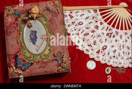 Un libro vintage con specchio e ventilatore sullo sfondo rosso Foto Stock