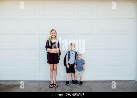 Tre bambini che posano davanti alla porta del garage con gli zaini. Foto Stock