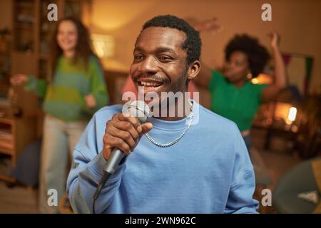 Ritratto in vita di un adulto nero che canta al microfono e sorride felici di godersi il karaoke a casa con gli amici Foto Stock