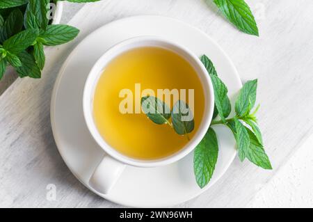 Tazza di tè alla menta con foglie di menta verde fresca su tavola rustica, sana bevanda calda a base di erbe Foto Stock