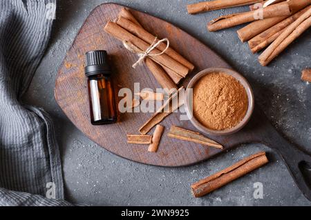 Bottiglia in vetro di olio essenziale di cannella con bastoncini di cannella e polvere su sfondo rustico scuro, medicina alternativa Foto Stock