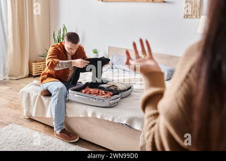 un uomo tatuato offeso che stava imballando la valigia vicino alla moglie litigando in camera da letto a casa, malinteso Foto Stock