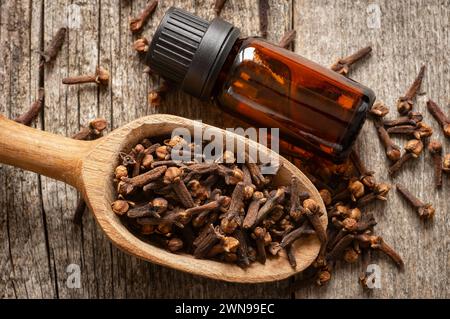 Chiudere una bottiglia di olio essenziale di chiodi di garofano e chiodi di garofano con una pala di legno o un cucchiaio sul tavolo di legno. Concetto di erbe e olio di spezie Foto Stock