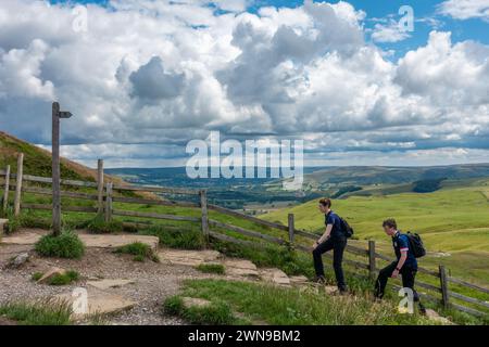 Due camminatori che camminano lungo i ripidi gradini sulla strada per Mam Tor in una giornata estiva con vista sul Peak District sullo sfondo nel Derbyshire, Regno Unito Foto Stock