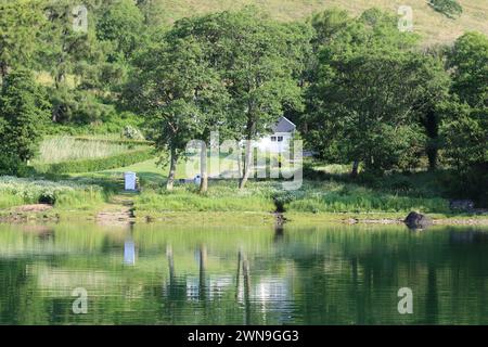 Cottage bianco su una sponda lacustre con alberi che si riflette nell'acqua ferma Foto Stock