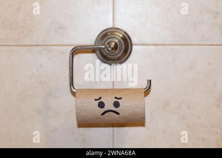 Centro di cartone di un rotolo di carta igienica senza carta con e faccia triste disegnata appesa a un supporto per rotolo di carta igienica Foto Stock