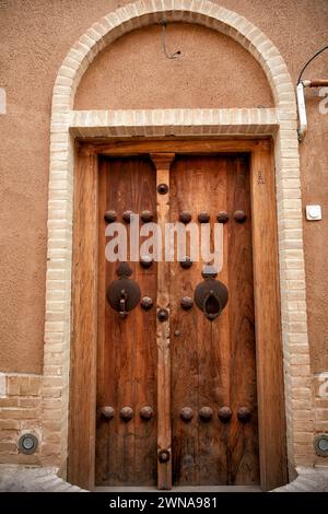 Vecchia porta d'ingresso in legno di una casa con due battitori separati - barra di metallo per uomini e anello di metallo per donne. Yazd, Iran. Foto Stock