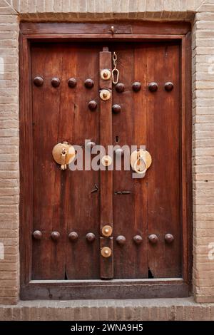 Vecchia porta d'ingresso in legno con due battitori separati - barra in metallo per uomini e anello in metallo per donne. Yazd, Iran. Foto Stock