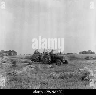 Anni '1960, storia, agricoltura, fuori in un campo, un trattore con un altro agricoltore su una pressa, una macchina imballatrice per fieno dietro, Inghilterra, Regno Unito. Foto Stock