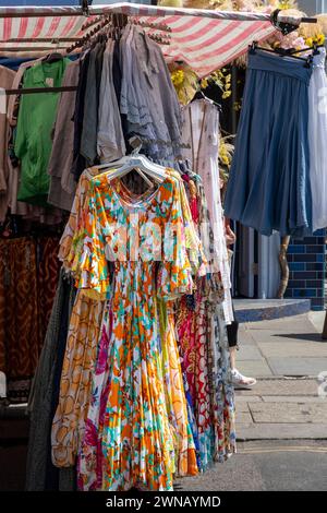 Abito dai colori vivaci e altri vestiti appesi su scaffale al mercato di Portobello, Londra, Inghilterra Foto Stock