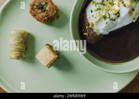 Primo piano di cioccolato bevuto in una tazza verde abbinata e piatto con panna e pistacchi e dessert baklava assortiti Foto Stock