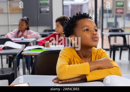 Il ragazzo birazziale in camicia gialla ha un aspetto premuroso in un'aula scolastica Foto Stock