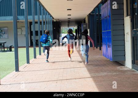 Tre bambini corrono attraverso un corridoio scolastico con armadietti sulla destra, con spazio per le copie Foto Stock