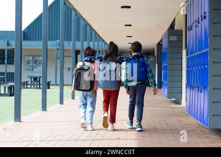 Tre bambini camminano lungo un corridoio scolastico, braccia l'uno sopra le spalle dell'altro Foto Stock